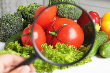 Woman with magnifying glass exploring vegetables, closeup. Poison detection