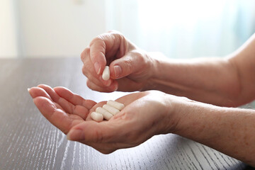 Elderly woman with pills in wrinkled hands. Medication in capsules, taking sedatives or vitamins