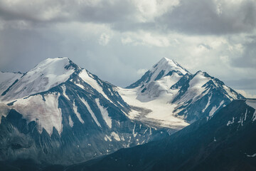 Dramatic mountains landscape with big snowy mountain ridge under cloudy sky. Dark atmospheric highland scenery with high mountain range in overcast weather. Awesome big mountains under gray clouds. - Powered by Adobe