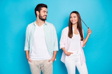 Portrait of two cheerful persons look each other hands in pocket lady play with hair isolated on blue color background