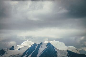 Dramatic mountains landscape with big snowy mountain ridge under cloudy sky. Dark atmospheric highland scenery with high mountain range in overcast weather. Awesome big mountains under gray clouds.