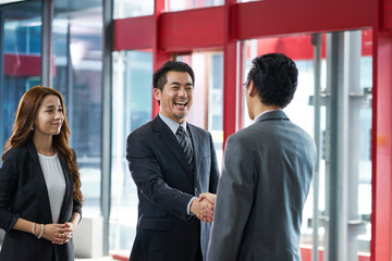 happy asian business people shaking hands in company lobby