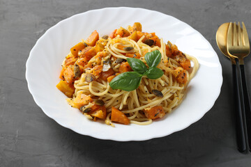 Spaghetti with pumpkin and pumpkin seeds in a white plate on a gray background. Closeup