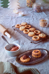 Sandwich cookies filled with hazelnut spread, nougat cream. Christmas Linzer cookies filled on cooling rack, metal plate. Winter decor, linen tablecloth.
