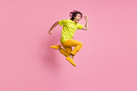 Full size profile photo of hooray curly hairdo guy jumping run wear t-shirt trousers sneakers isolated on pastel pink background