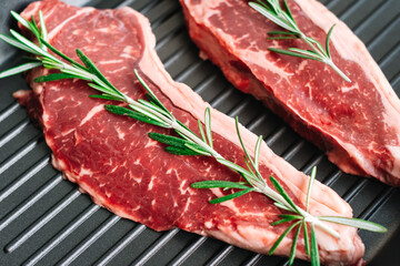 Raw beef steak with rosemary in black grill pan on the table. Close-up