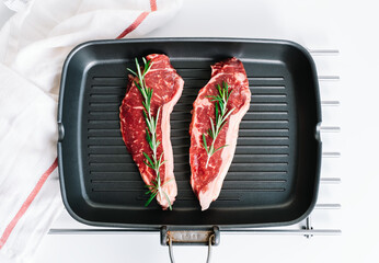 Raw beef steak with rosemary in black grill pan on the table.
