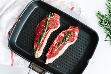 Raw beef steak with rosemary in black grill pan on the table.