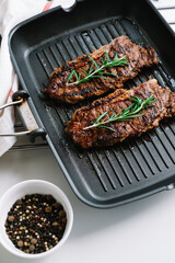 Grilled beef steak with rosemary in black grill pan on the table.