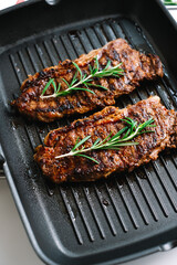 Grilled beef steak with rosemary in black grill pan on the table.
