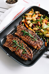 Grilled beef steak with vegetables and rosemary in black grill pan on the table.