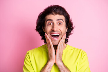 Photo portrait of surprised excited man smiling touching cheeks isolated on pastel pink color background