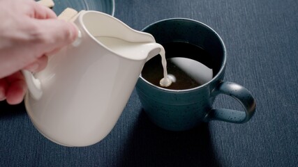 Adding cream to a blue cup on a table. Milk coffee. Dark blue background