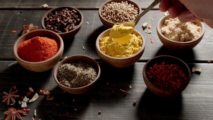 Human hand takes by the spoon a spices in variety of colourful seasoning on a table