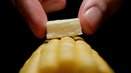 Man puts a piece of butter on sweetcorn cob. Close up.