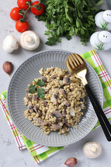 Homemade ptitim pasta with champignons in a plate on light gray table. Vertical format. View from above