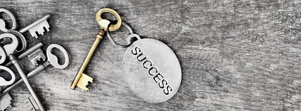 success engraved on a ring of an golden old key on wooden background with other silver
