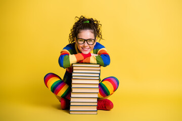 Photo of diligent student lady sitting floor lean book pile legs crossed wear striped rainbow clothes isolated yellow color background