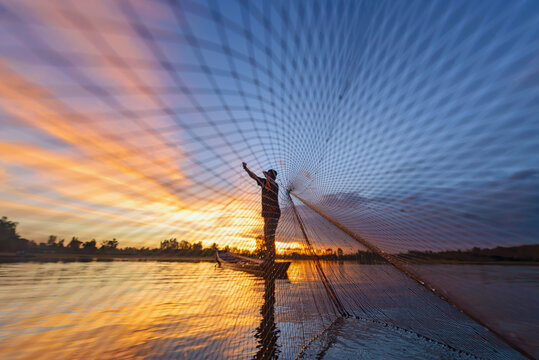 Fisherman casting his net on during sunrise.Silhouette Asian fisherman on wooden boat casting a net for freshwater fish