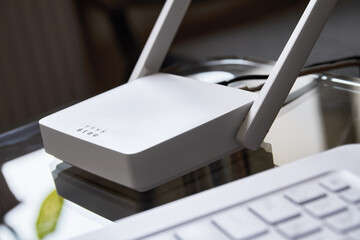 White wireless wi-fi router near a laptop on a glass table