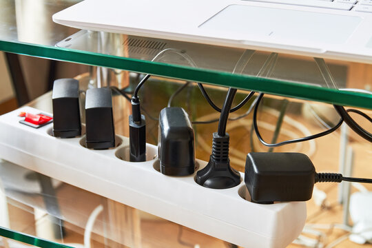 Electrical Power Strip Overloaded With Multiple Electrical Cords Plugged In. Many Plugs Plugged Into Electric Power Bar