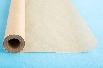 Rolled out roll of baking paper on light blue table background. Pastel color. Closeup. Empty place for text.