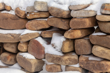 Stacked stones, covered with snow. A wall of stones.