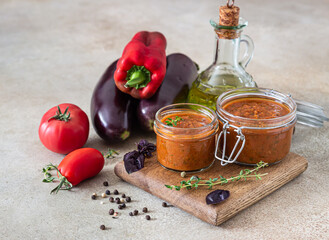 Vegetable caviar in jar, fresh eggplants, bell pepper, tomatoes and thyme on wooden board. Homemade preserves. Vegetarian cuisine. Autumn harvest.