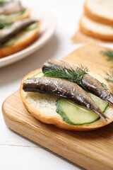 Delicious sandwich with sprats, cucumbers and dill on wooden board, closeup