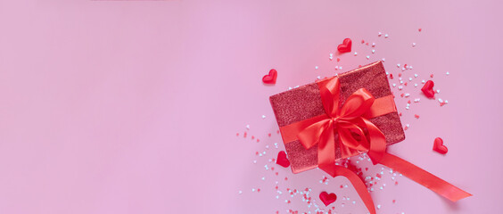 Gift red box with red bow ribbon and hearts on pink background for Valentines day. Space for text. Long wide banner.