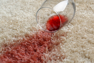 Overturned glass and spilled red wine on soft carpet, closeup