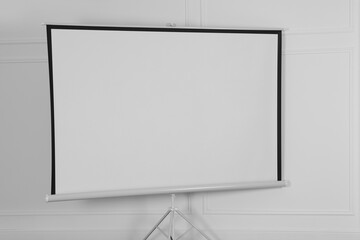 Obraz premium Blank projection screen near white wall indoors. Space for design