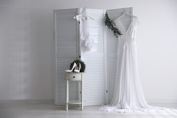 Wedding dress, high heel shoes and veil near white wall indoors