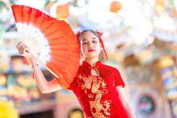 Portrait beautiful smiles Cute little Asian girl wearing red traditional Chinese cheongsam decoration and holding a Fanning for Chinese New Year Festival at Chinese shrine