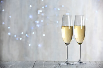 Sparkling wine in glasses on wooden table against blurred lights, space for text