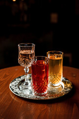 Two long drink cocktails with ice in vintage highball glasses and a glass of wine or vermouth on a silver tray