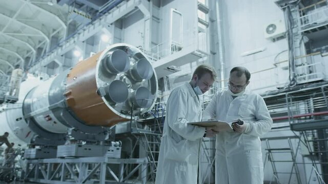 Two scientist engineers inspect the spacecraft, write on the tablet. A space rocket in a military hangar being prepared for launch. Space technologies. Construction of Big Rocket. Humanity in Space