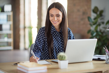 Photo of happy focused young businesswoman sit desk write note wear formalwear in office indoors...