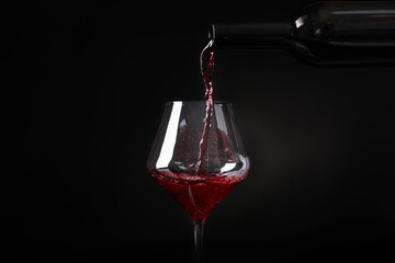 Fototapeta na wymiar Pouring wine from bottle into glass on black background