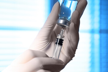 Woman filling syringe with vaccine from vial on blurred background, closeup