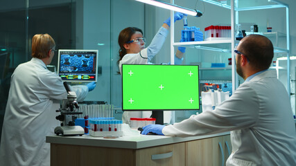 Scientist man typing on computer with green mockup in modern equipped lab working late at night. Team of microbiologists doing vaccine research writing on device with chroma key, isolated display.