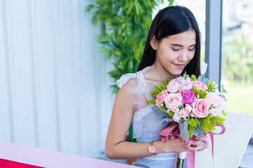 Valentine's day concept, Happy of smiling Asian young female sitting at a table food holding a bouquet of roses at in the restaurant background