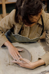 A young Caucasian woman makes sides with her hands for a plate of clay in a pottery workshop. Beautiful dishes with their own hands. Manual labor. Creative masterclass