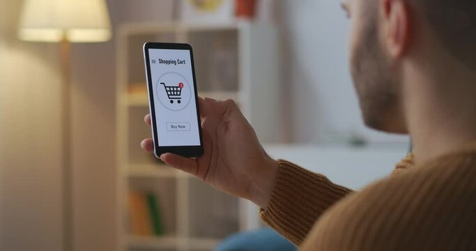 man is buying online by smartphone, tapping on touch screen, paying by card, graphics on display, view through shoulder