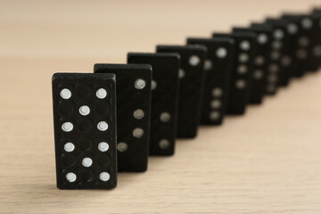 Black domino tiles with white pips on wooden table, closeup
