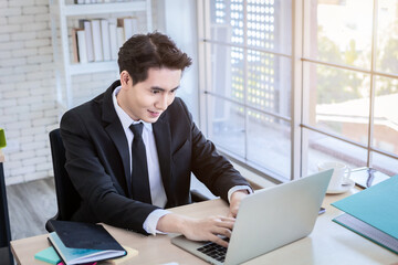 Happy of asian young businessman see a successful business plan on the laptop computer and pen on wooden table background in office,business expressed confidence embolden