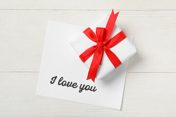 Card with text I Love You and gift box on white wooden table, top view