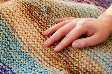 The woman's hand lies on knitted multicolored handmade plaid, close-up, creative background.