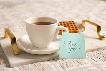 Paper note I Love You near cup of morning drink and waffle on bed. Romantic breakfast