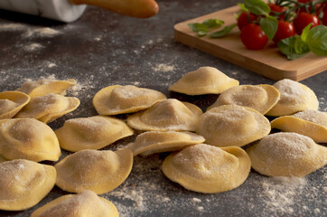 homemade stuffed pasta and table with tomatoes and basil on blur background